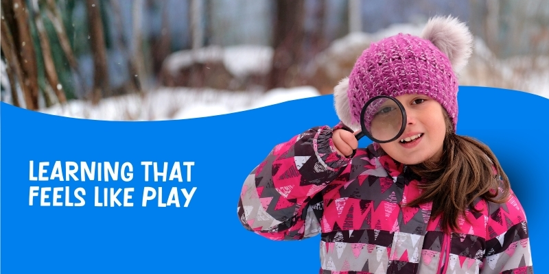 young girl wearing a pink toque with grey pom-poms looking through a magnifying glass