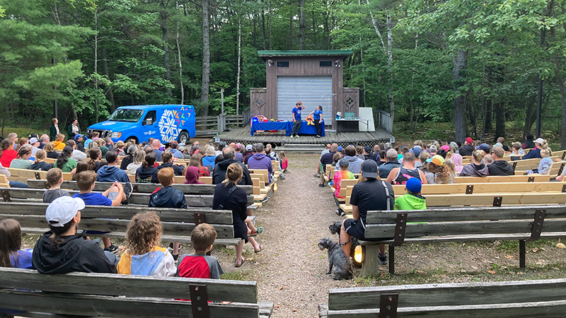 example of an outreach live show — large group of kids in a park area listening to a presentation by two bluecoats on stage
