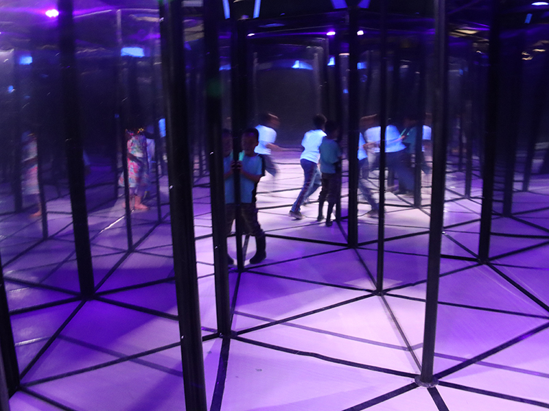 several kids having fun attempting to navigate through the multitude of mirrors in the mirror maze